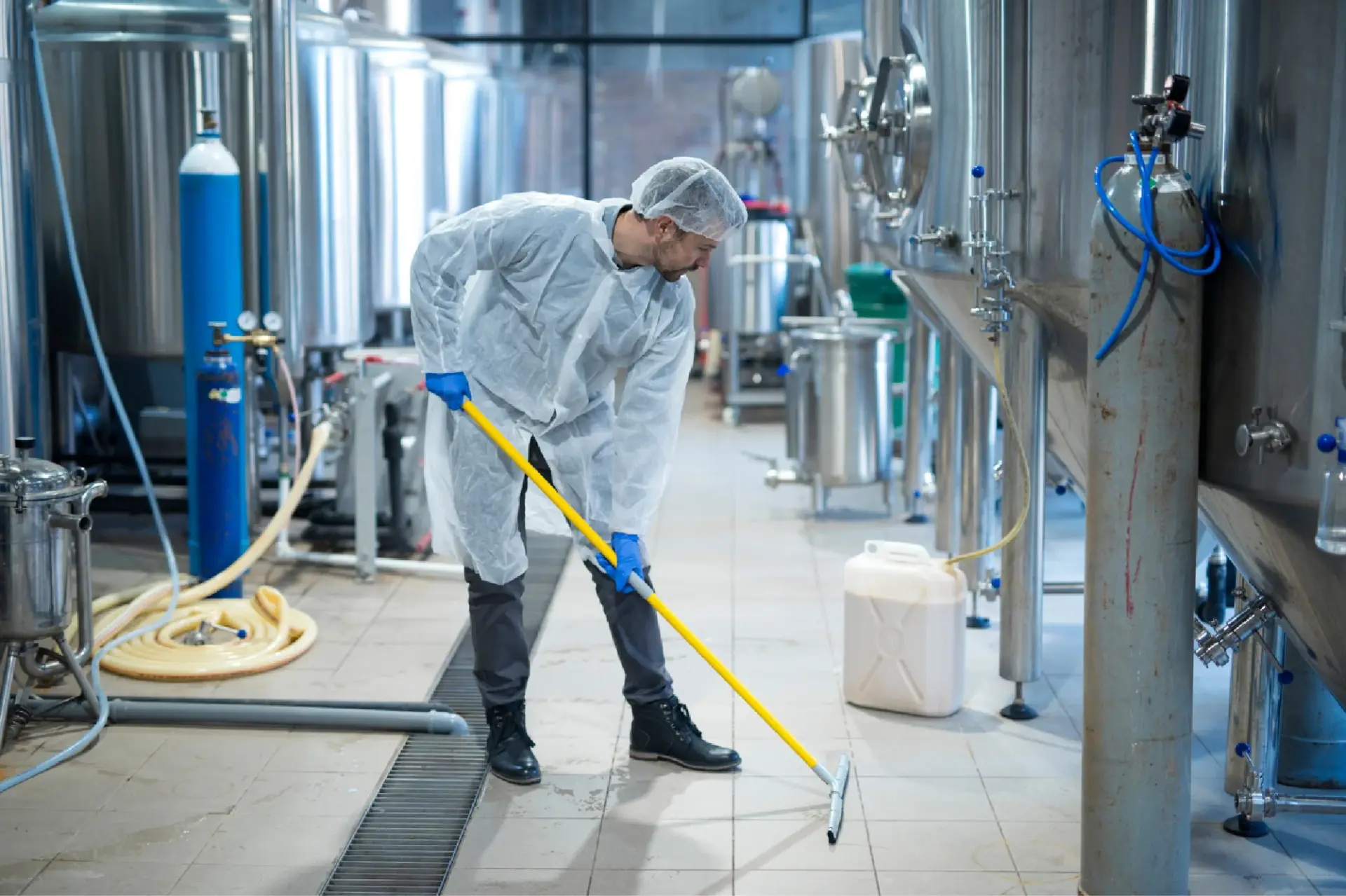 Cleaner in protective clothing sanitising an industrial floor
