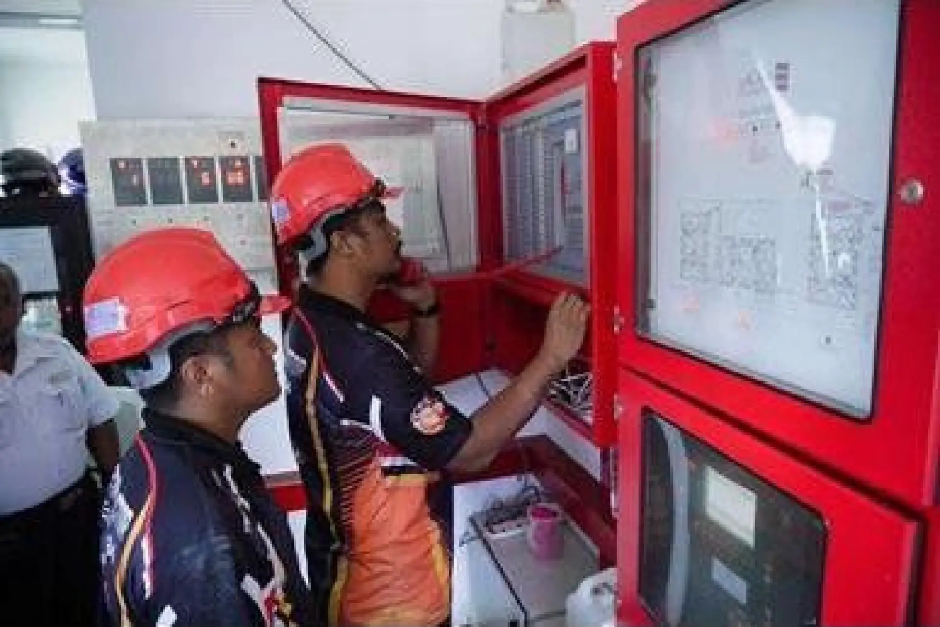 Technicians in hard hats inspecting a fire control panel